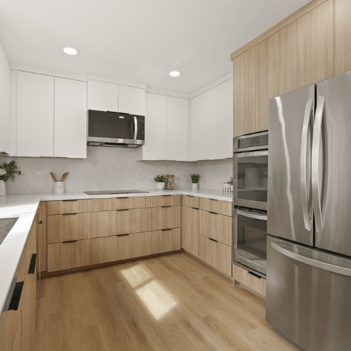 Bright modern kitchen with white upper cabinets, light wood lower cabinets, and stainless steel appliances