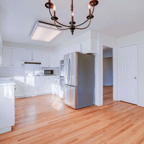 Bright kitchen with white cabinets, stainless steel fridge, skylight, and hardwood floors