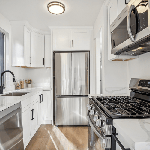 Bright white modern kitchen with stainless steel appliances, gas stove, and natural light.