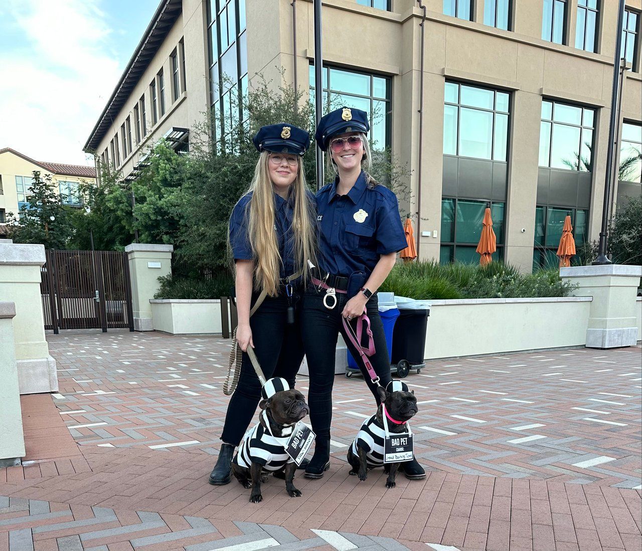 Two police officers on patrol with small dogs outside a building.