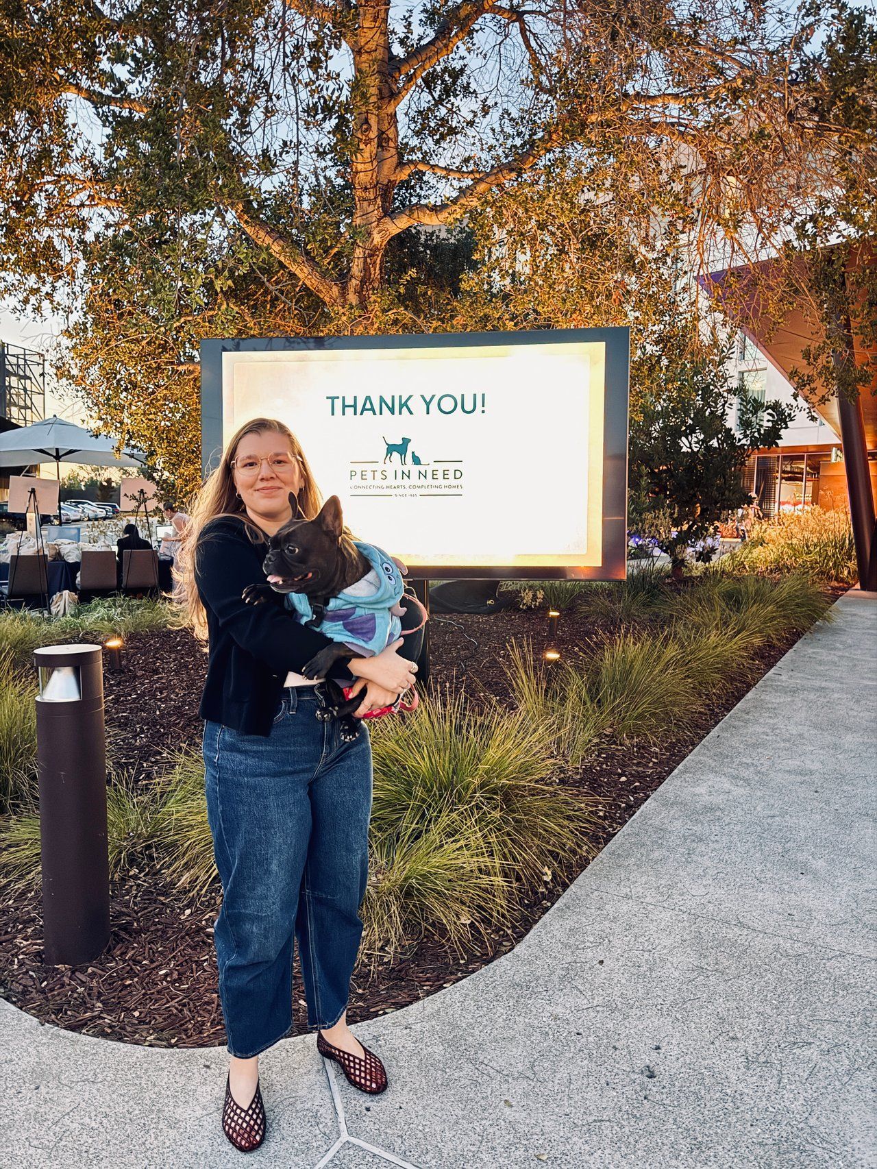 Woman holding a cat stand beside a “Thank You” sign on a walkway outdoors.