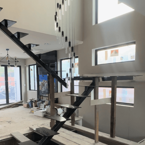 Modern interior with open staircase, hanging pendant lights, and large windows under construction