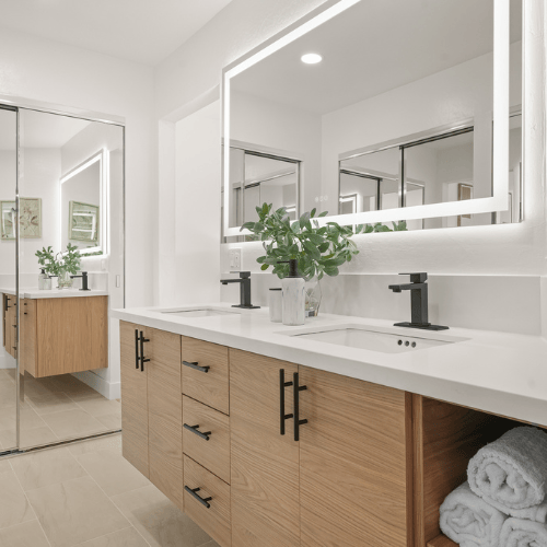 Modern bathroom with light wood vanity, white countertops, large mirror, and folded towels