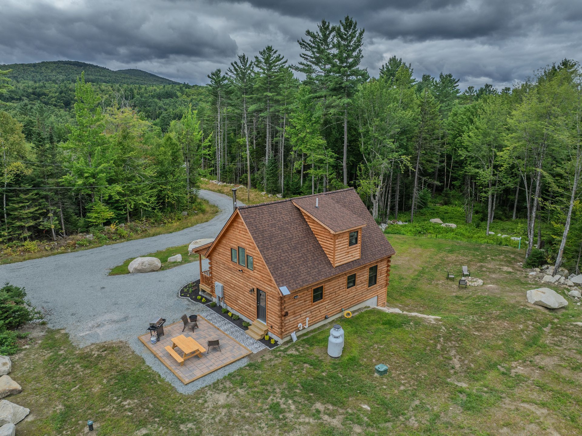 Rustic cabin with brown siding, shingled roof, and gravel driveway, set in a wooded area.