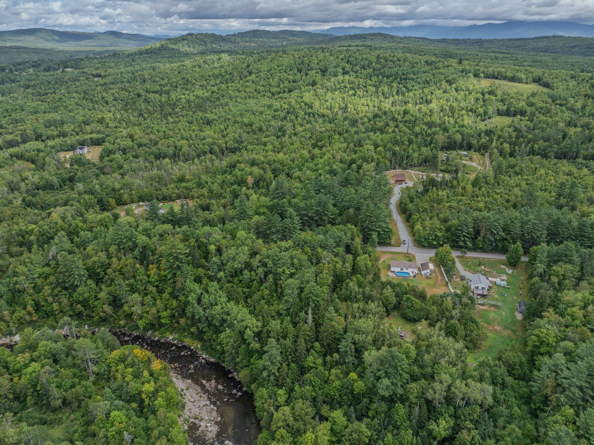 Aerial view of lush green forest and a small neighborhood with houses. A river runs through the trees.