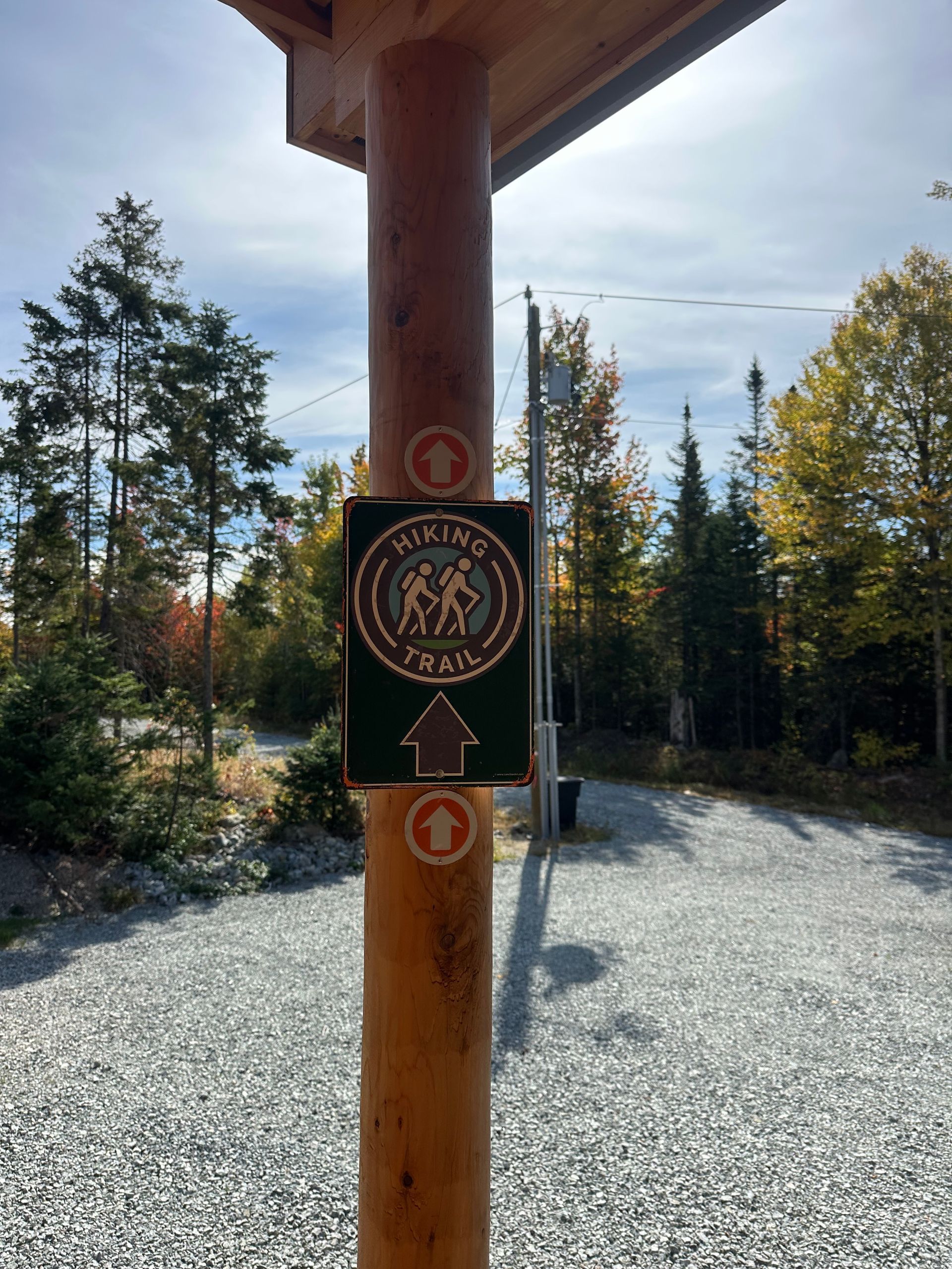 Hiking trail sign on a wooden post, with directional arrows. Green sign with white hiker silhouette.