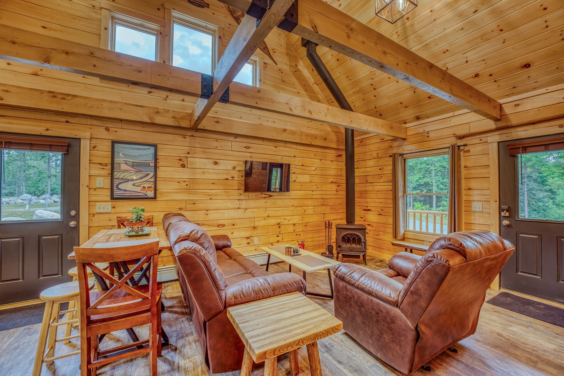 Cozy cabin interior with wood paneling, leather recliners, a small wood stove, and a bar table.