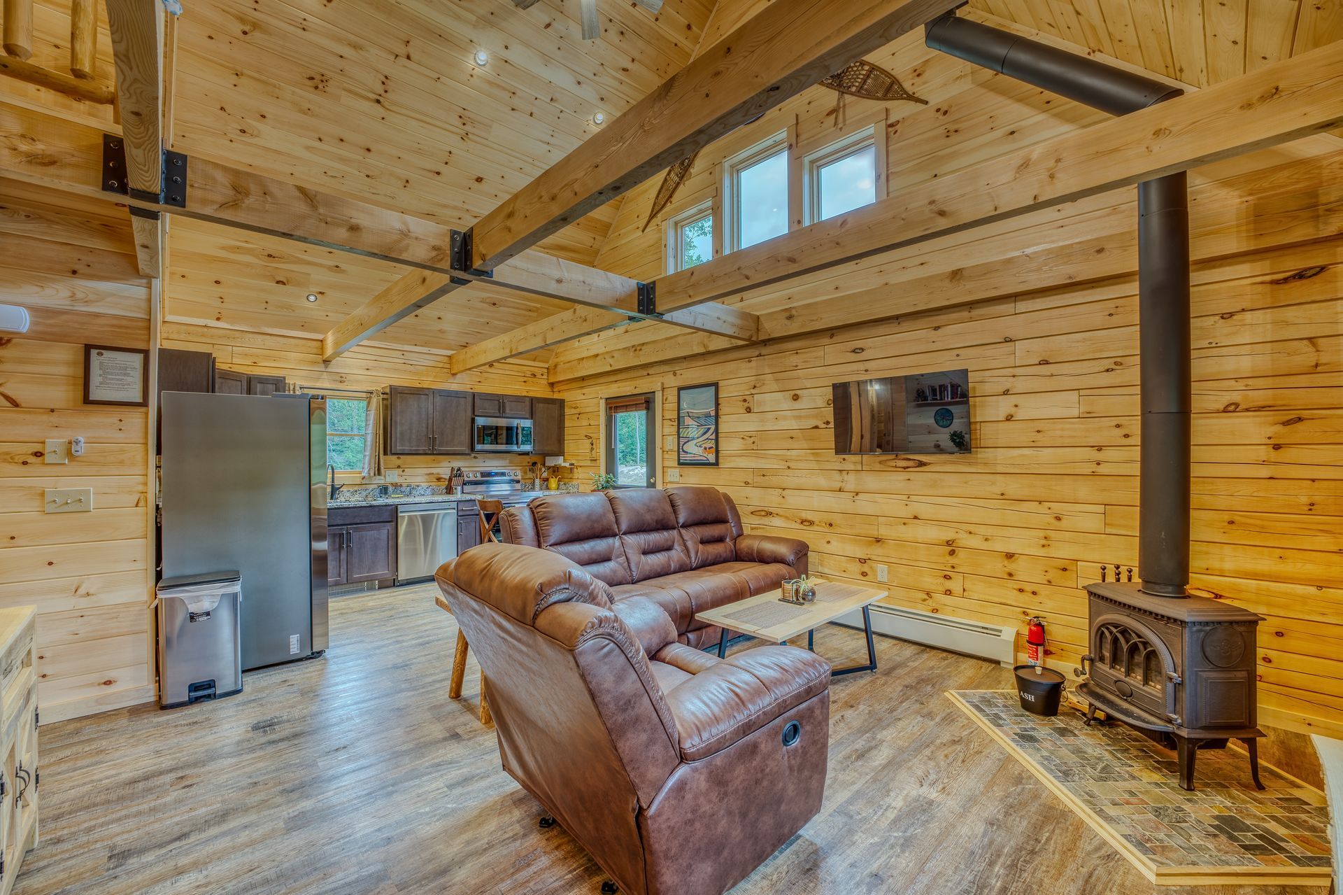 Interior of a wooden cabin living room with a brown leather sofa, fireplace, and kitchen in the background.