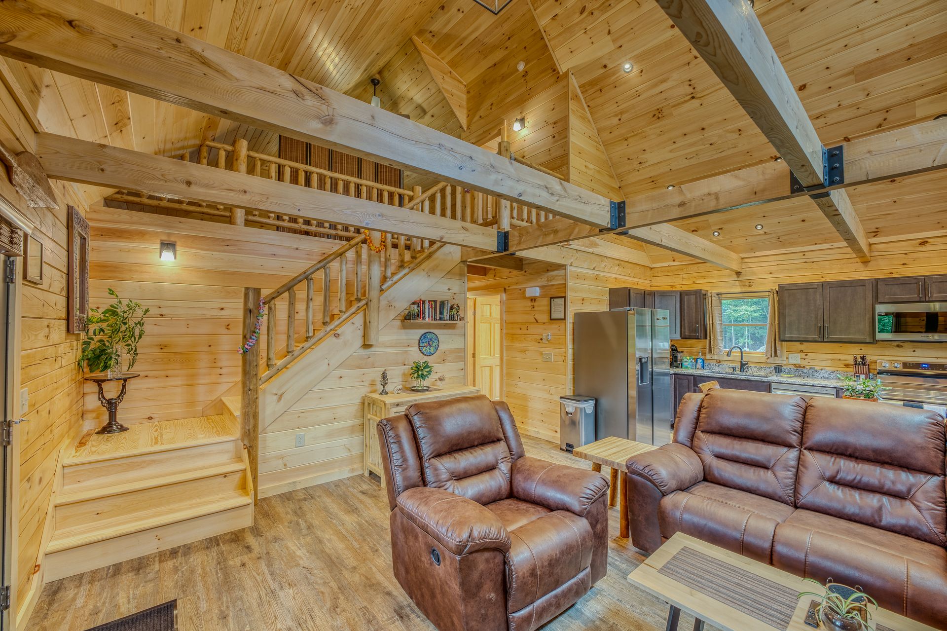 Cozy cabin interior with wooden walls, leather furniture, and loft area.