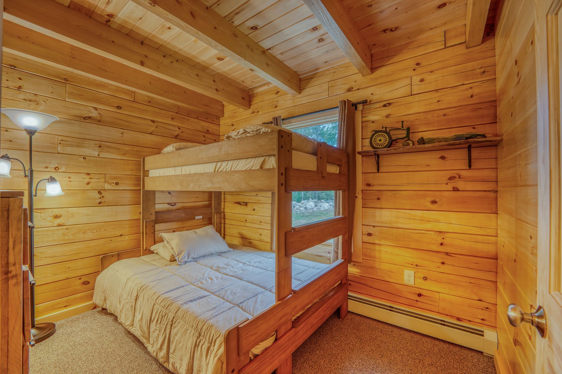 A small wood-paneled bedroom with a bunk bed, window, and decorative shelf.