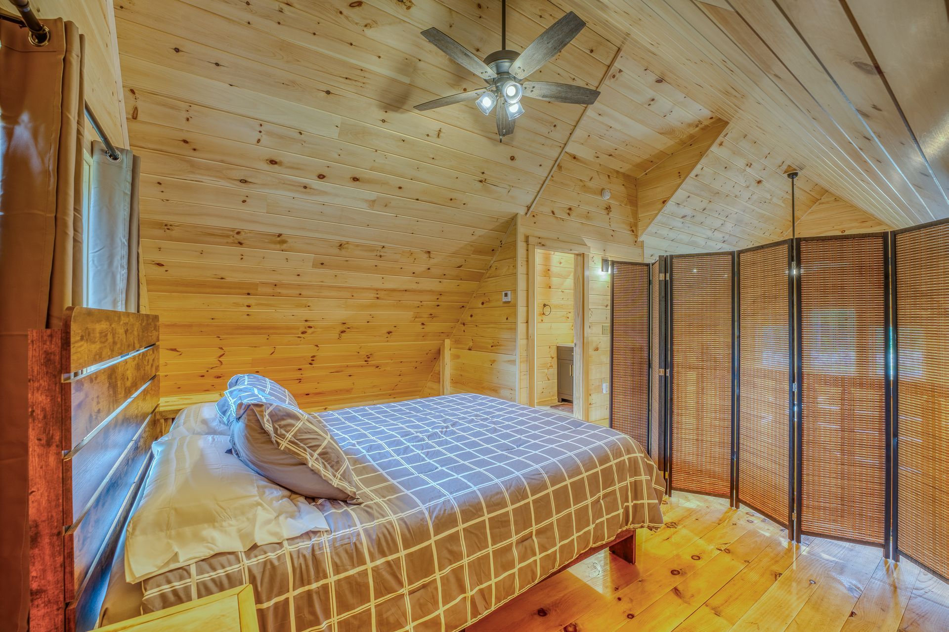 Bedroom with wood paneling, bed with patterned cover, and a folding screen.