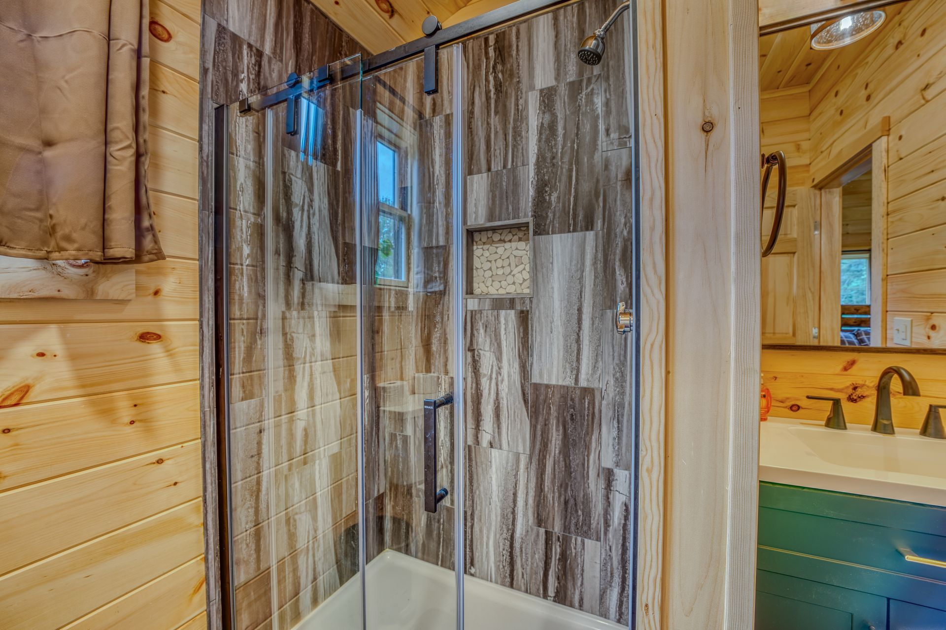 Bathroom with wooden walls, glass shower, and wood-look tile. Vanity with mirror and sink.