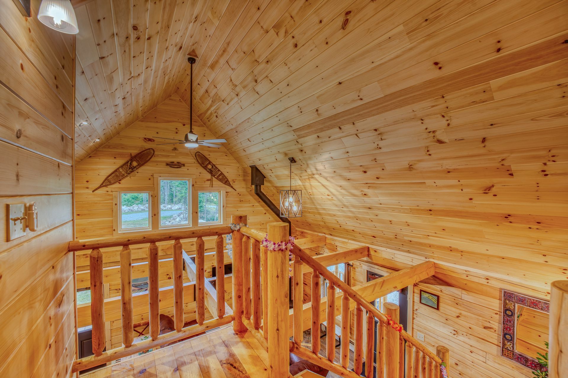 Wooden cabin interior with a second-floor railing, stairs, and a ceiling fan.