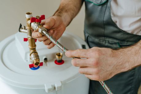 Plumber tightening a brass water heater valve with a wrench on a white tank under repair