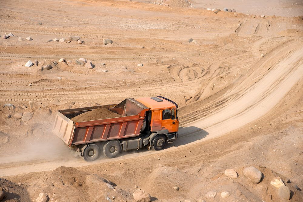 A Dump Truck Is Driving Down A Dirt Road — Macquarie Valley Rock & Sand In Warren, NSW