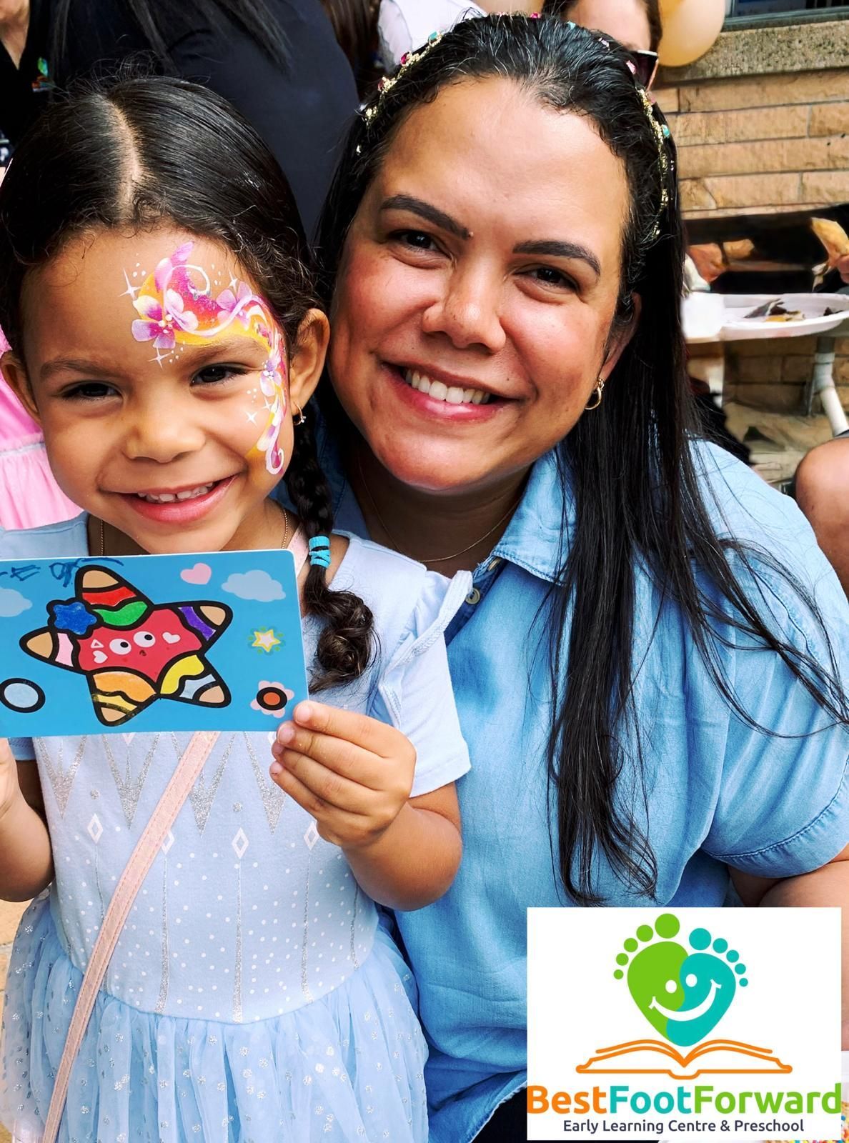 Smiling woman and child holding a colorful fish craft, with a Best Foot Forward logo in the corner