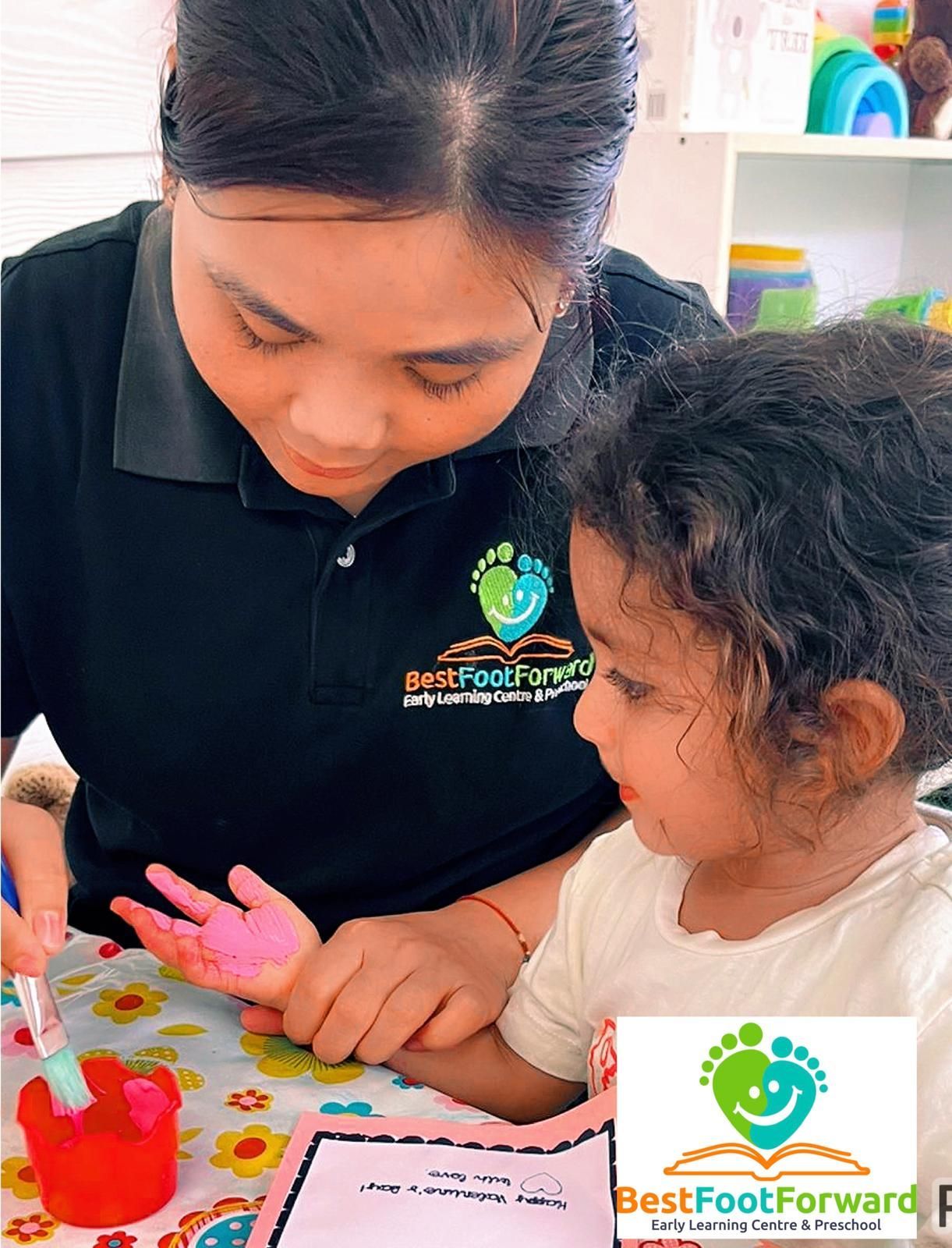 Teacher and child painting together at a table with colorful art supplies and handprints.