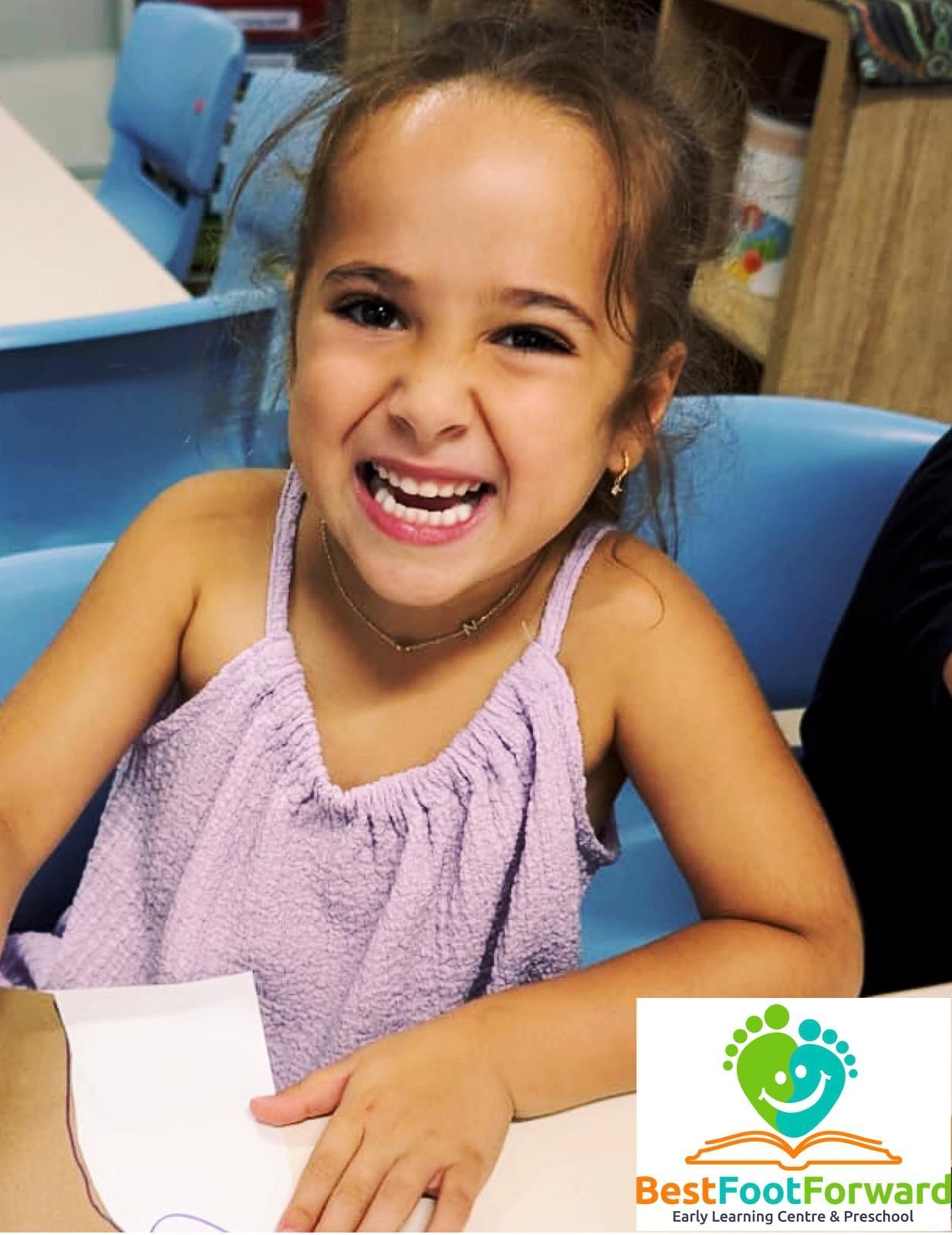 Smiling child in a lavender top at a table, with the Best Foot Forward logo in the corner