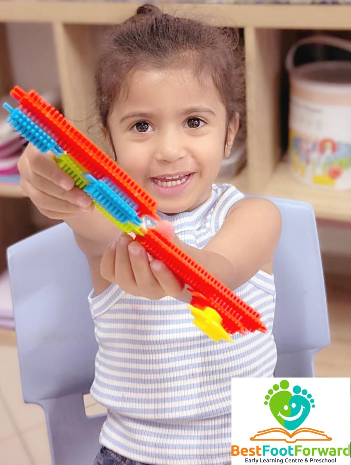 Smiling child holding a colorful toy rod in a playroom