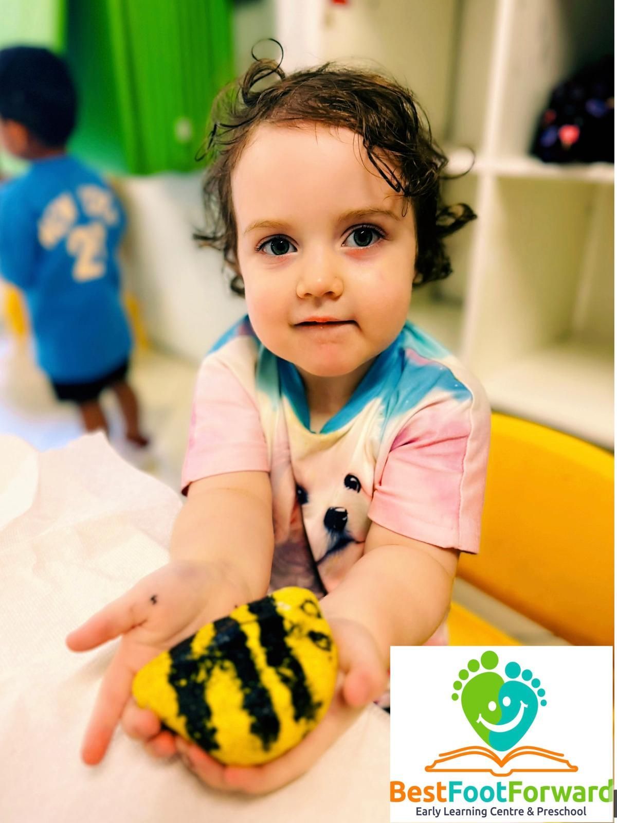 Toddler reaching out with a yellow-and-black striped toy in a bright indoor play area