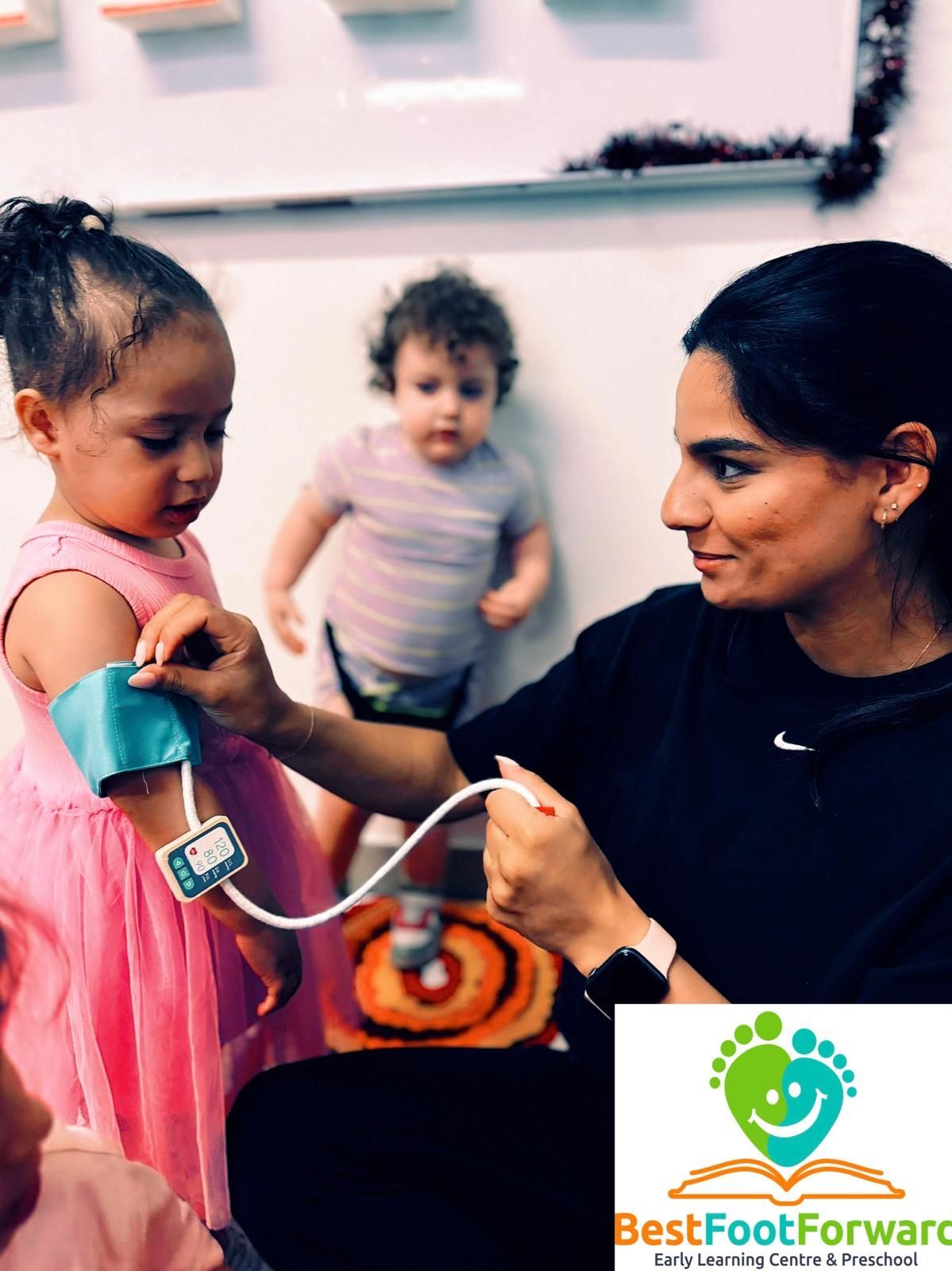 Woman fitting a pink prosthetic leg on a child in a clinic, with another child nearby