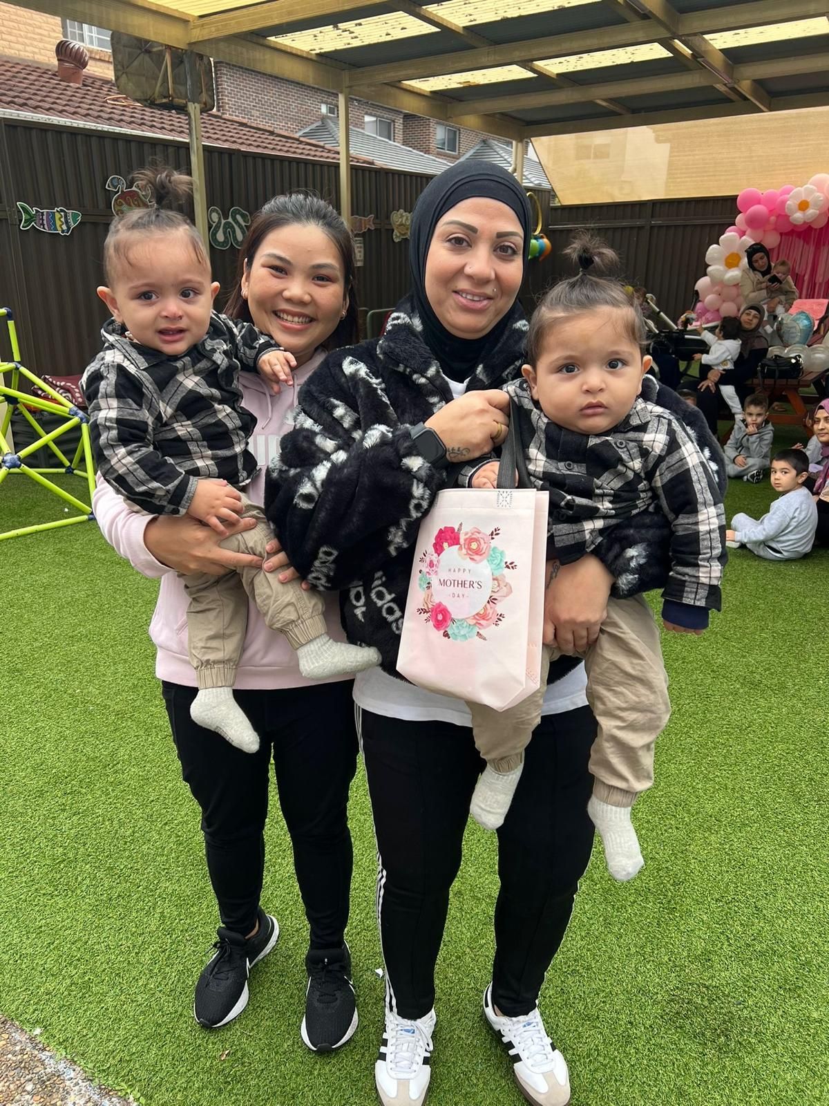 Three people holding two toddlers stand on green turf inside a covered event space.