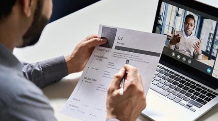 Person reviewing resume during a video interview on a laptop.