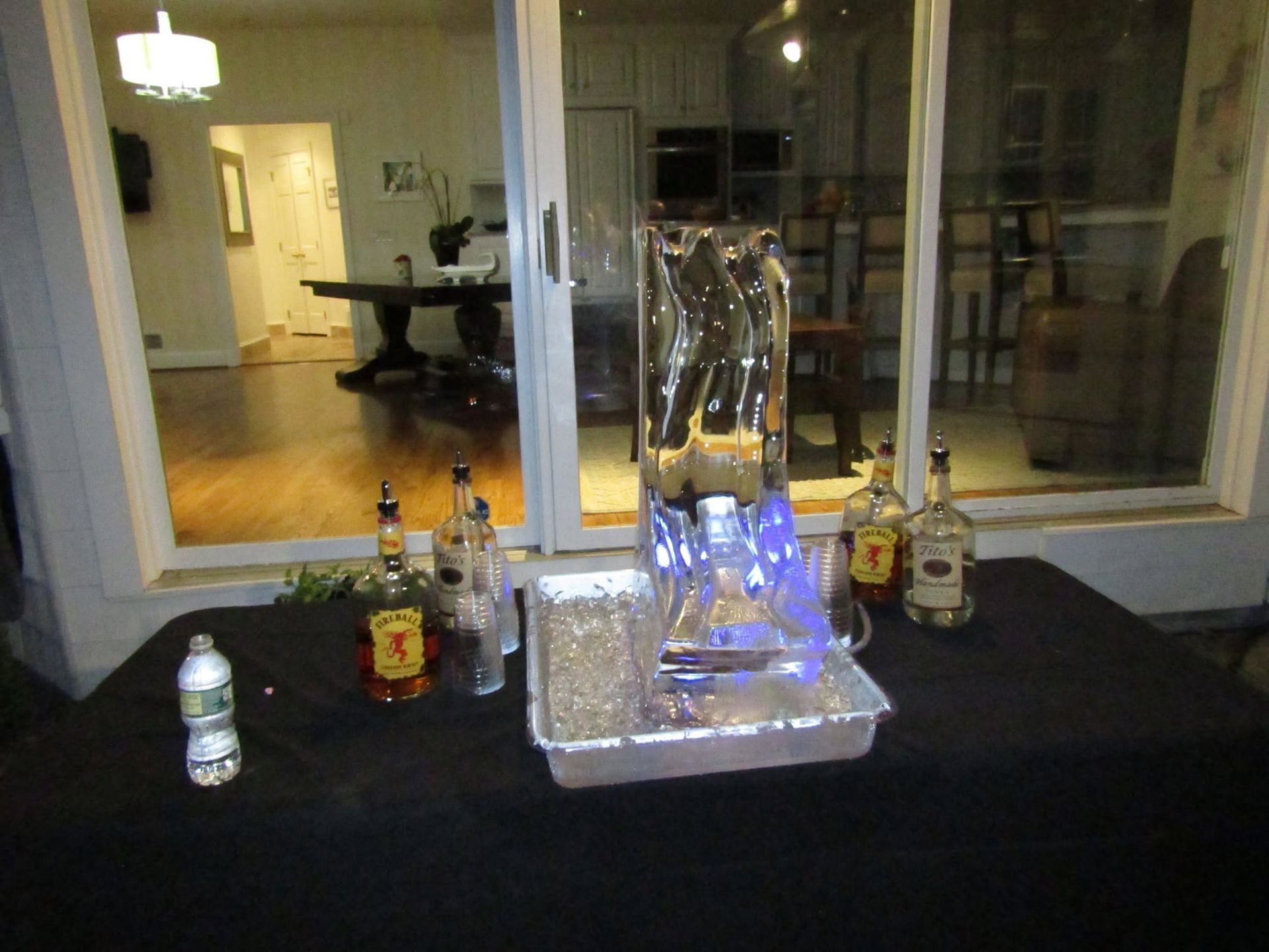 Ice sculpture with blue lighting on a table, surrounded by liquor bottles in a dim indoor setting