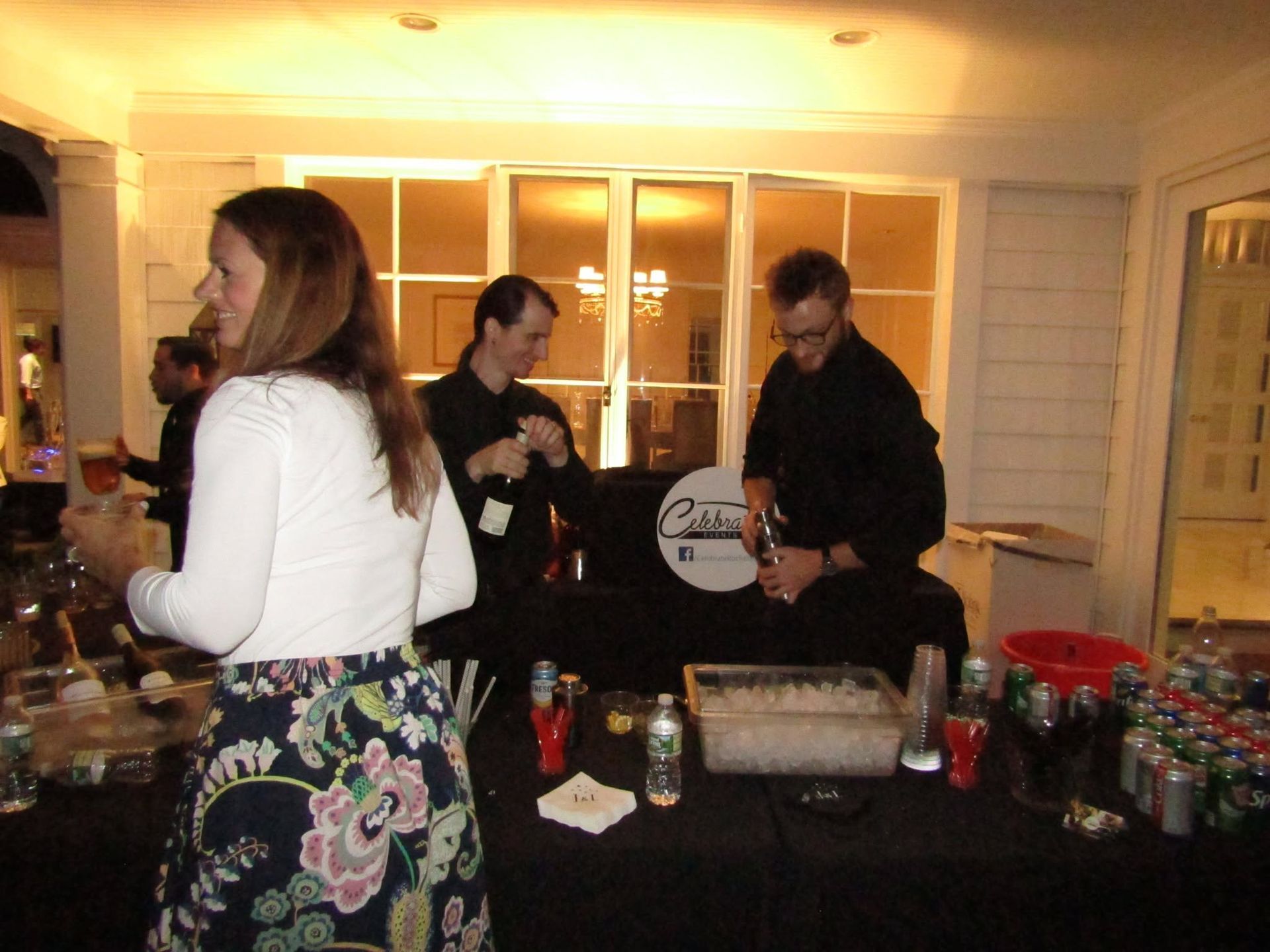 People gathered around a buffet table at an outdoor evening event, with drinks and food trays on display.