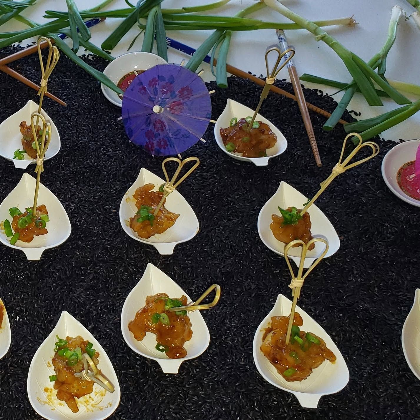 Small white spoons of plated appetizers on black slate, garnished with herbs and topped with orange relish.