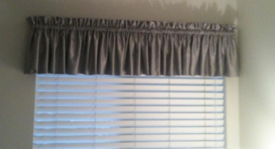 Gray fabric valance over a window with closed blinds.