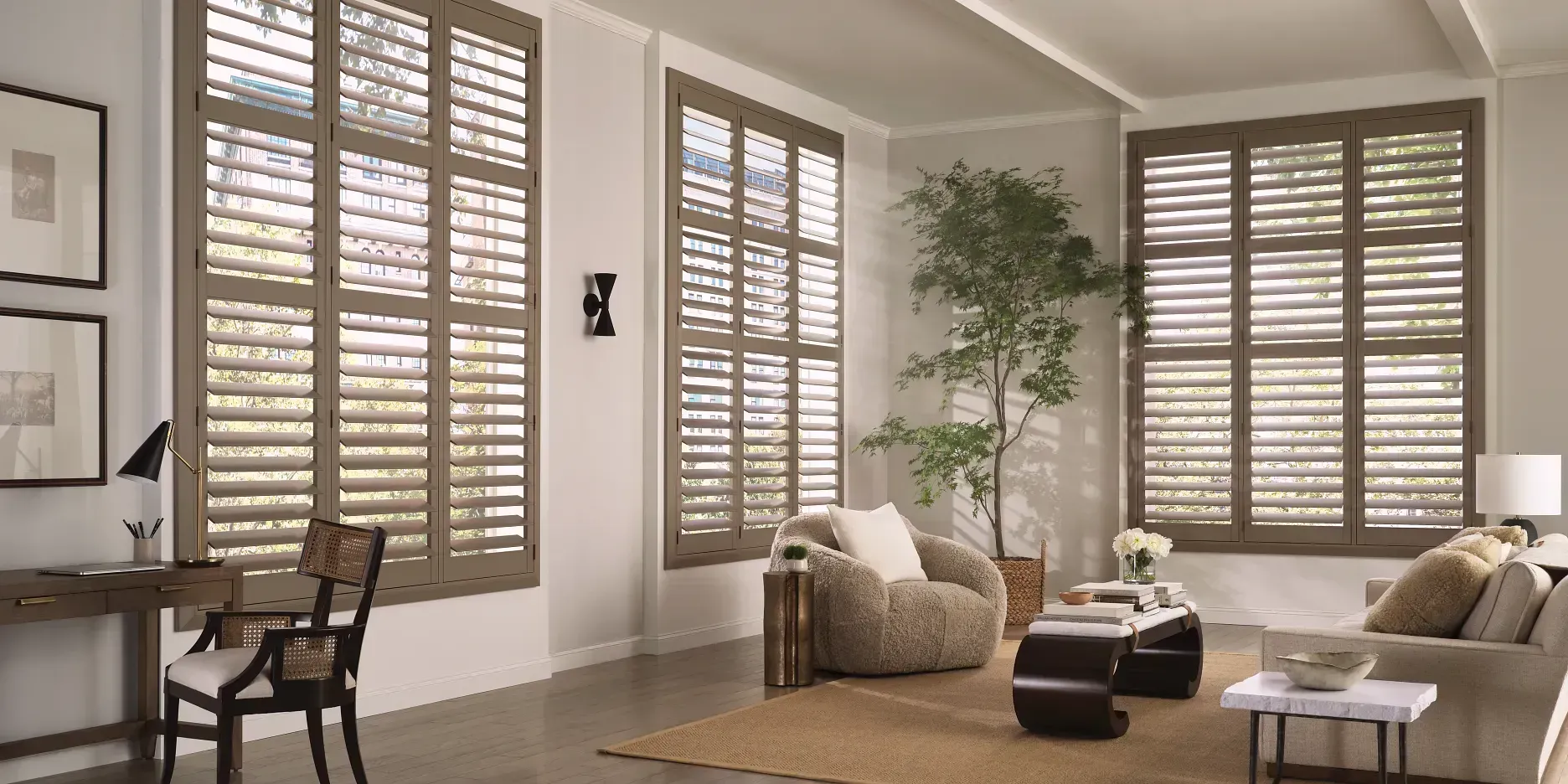 Living room with large windows, brown shutters, a desk, and a couch.