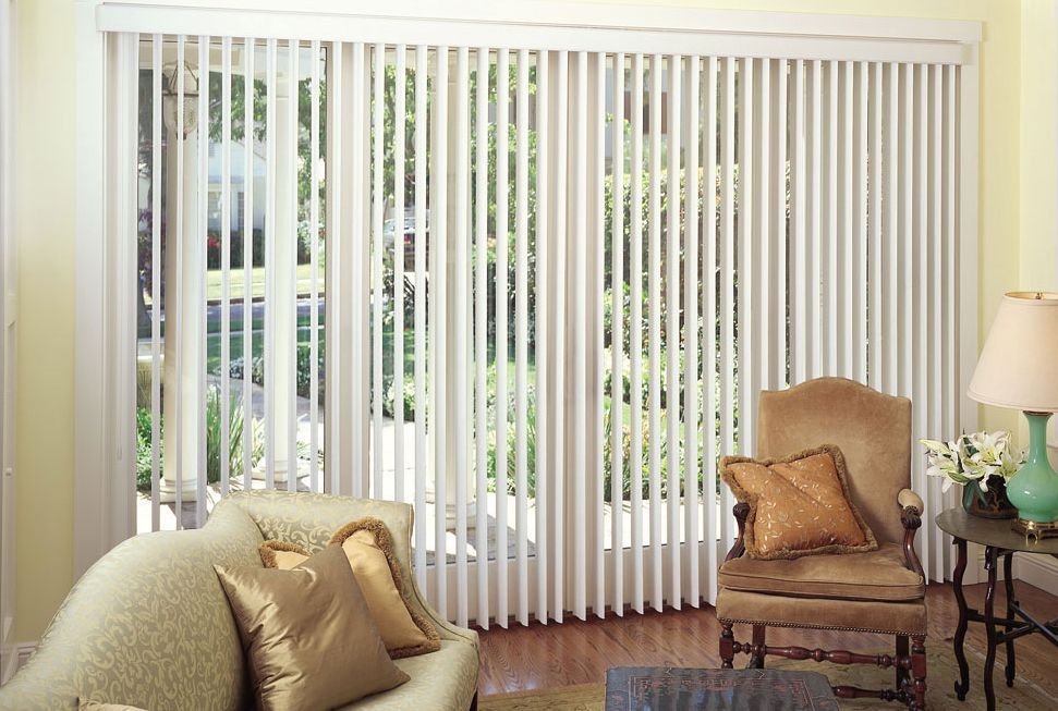 Living room with vertical blinds, chair, sofa, and a table with a lamp.