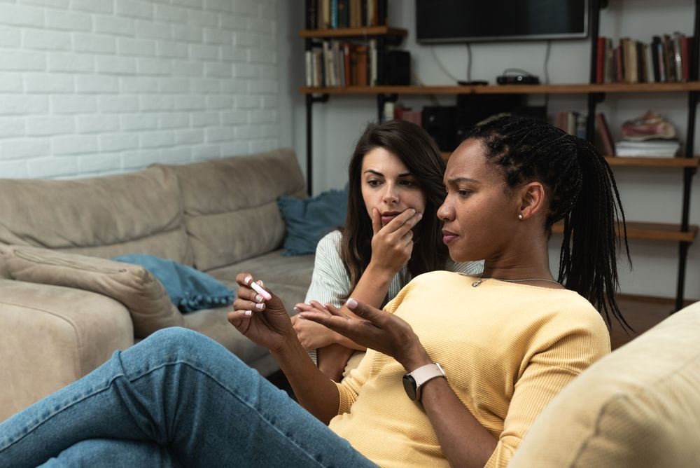 Two people on a couch, looking at a pregnancy test in a living room