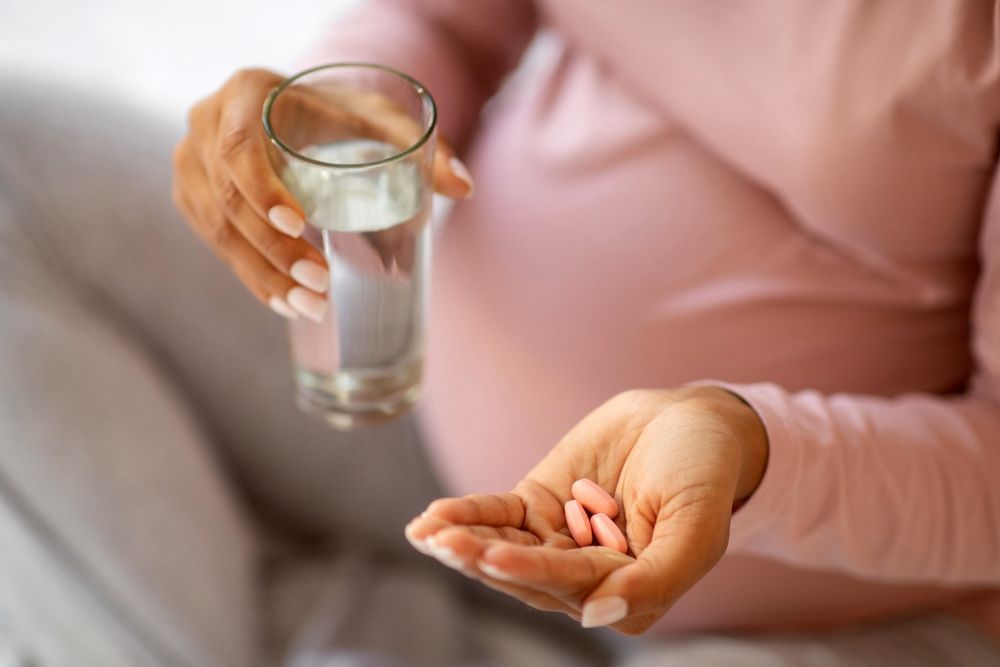 A pregnant woman holding a glass of water and prenatal vitamins.