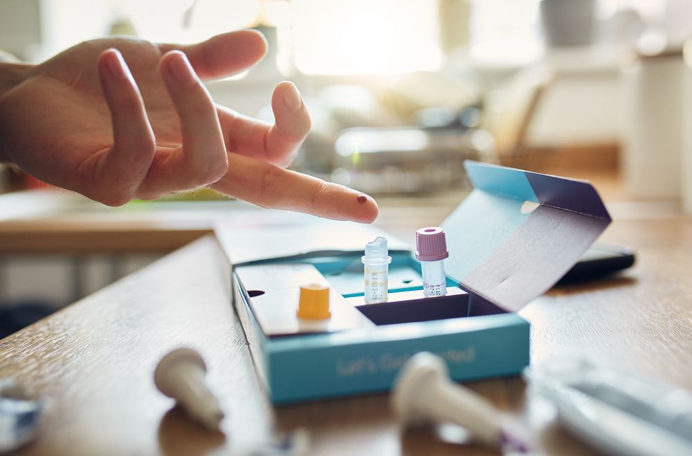 Person taking a finger-prick blood test at a table, with test kit.
