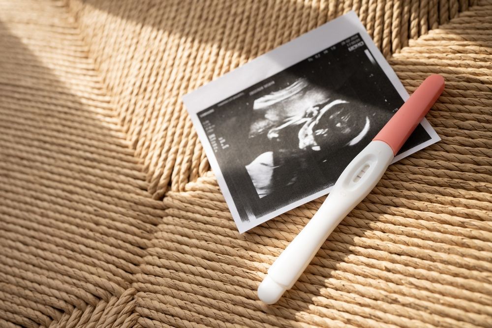 Positive pregnancy test beside printed ultrasound image on woven mat.