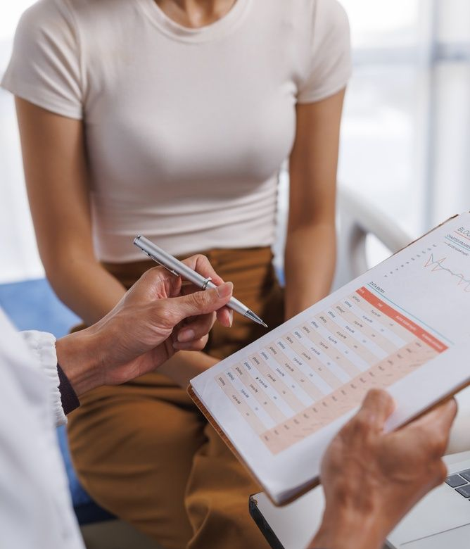 Healthcare professional reviewing notes on a clipboard with a seated patient in a bright clinic.