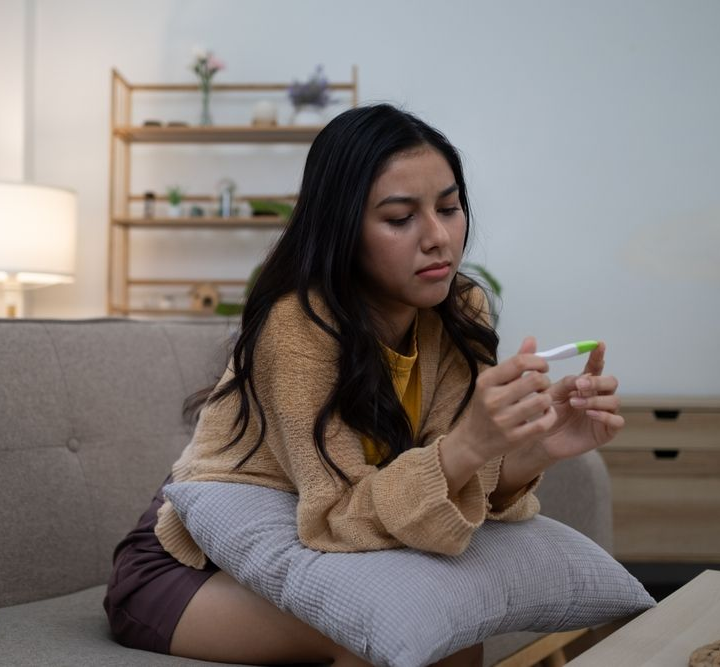 A pensive young woman staring at a pregnancy test.