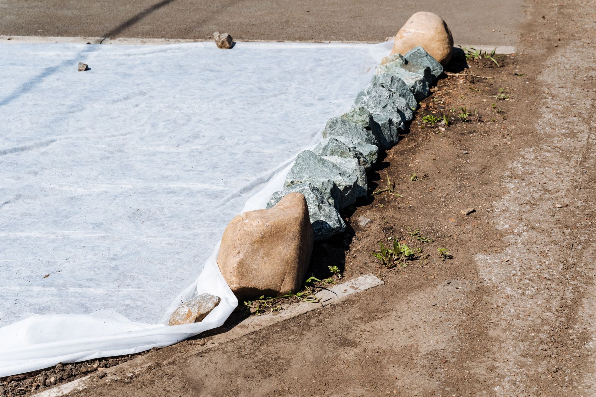 Plastic sheeting held down by rocks along the edge of a dirt path outdoors