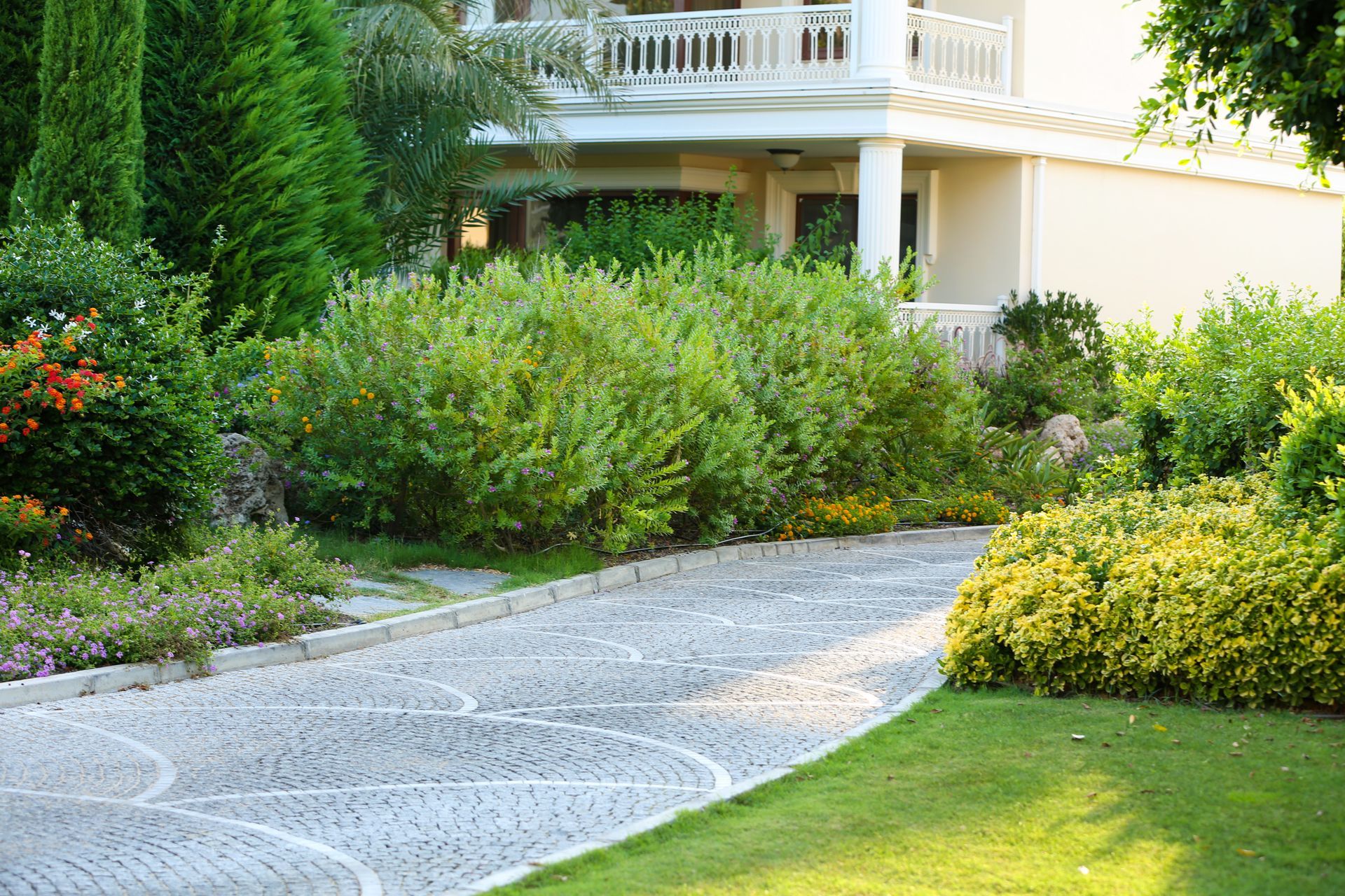 Curved garden path beside lush shrubs and a white house with a porch