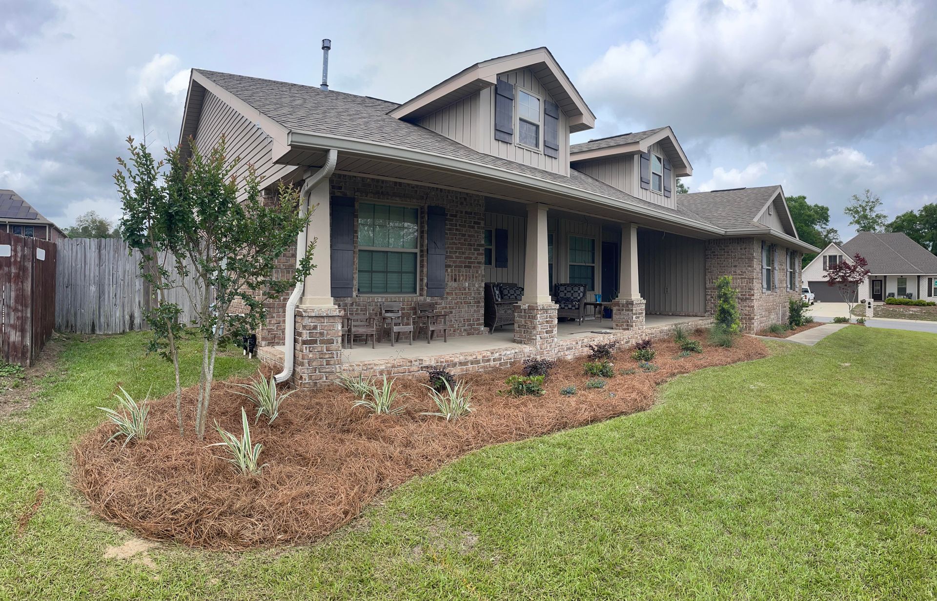 Single-story brick house with a covered porch, front lawn, and landscaped yard under cloudy skies