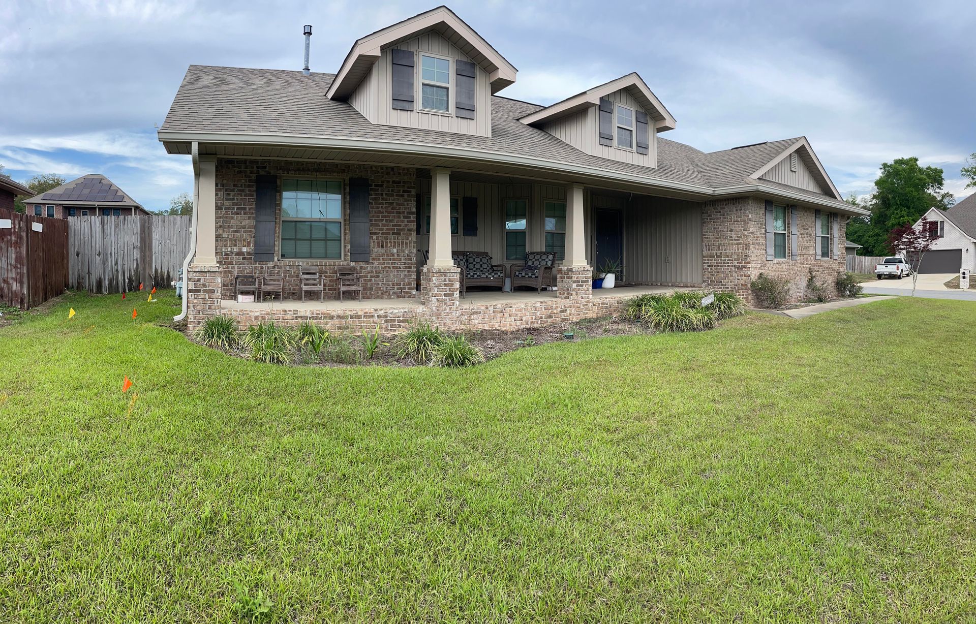Stone suburban house with covered front porch and large green lawn under cloudy sky