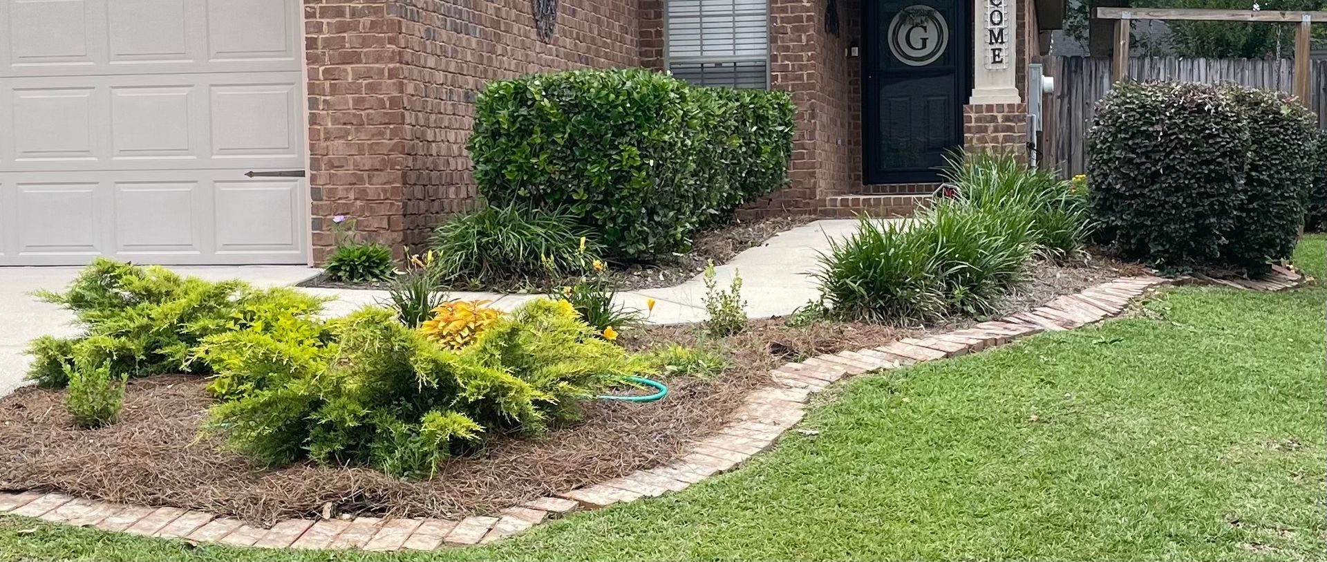 Mulched front yard landscape with shrubs and a brick house entrance