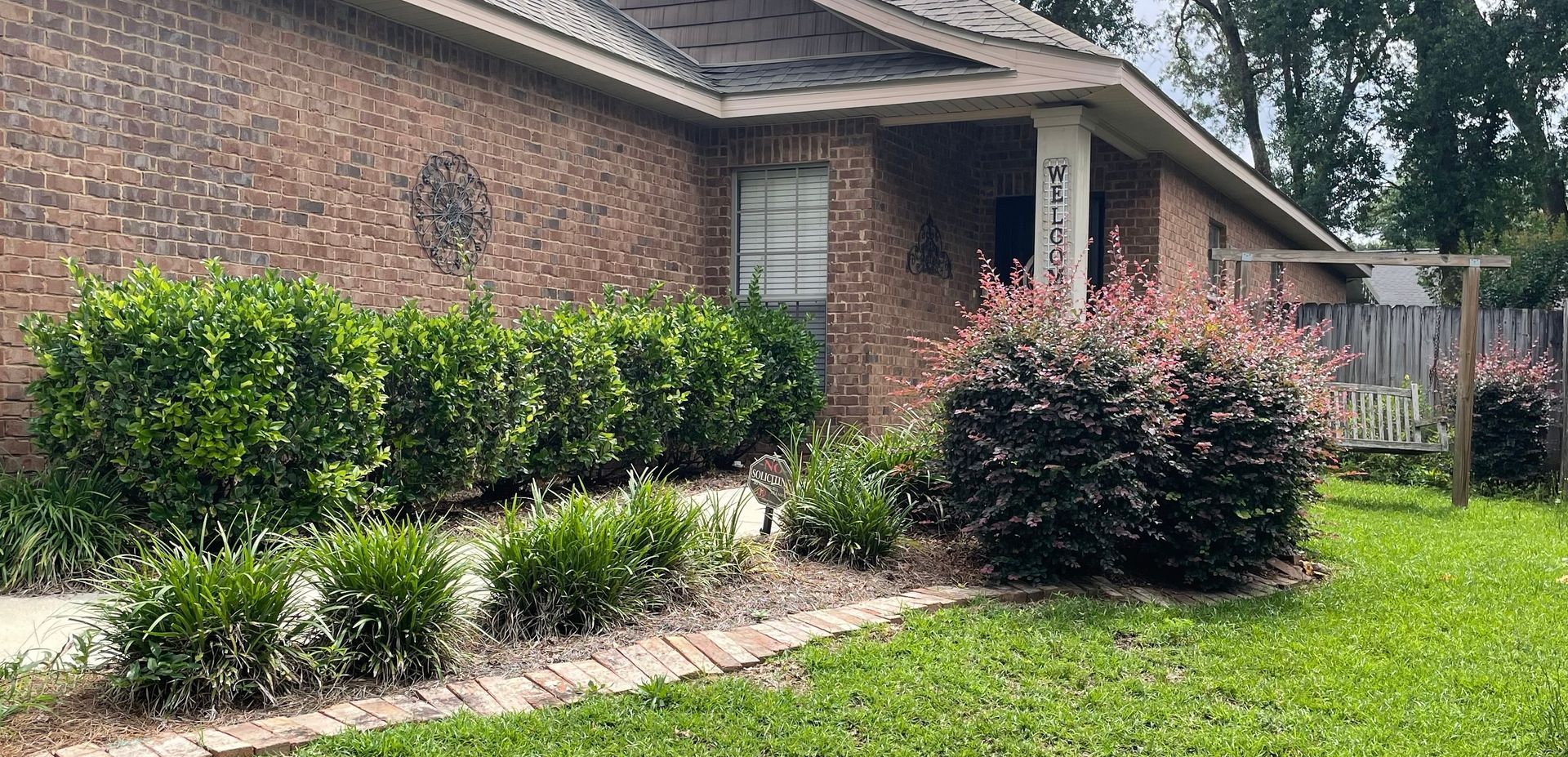 Brick house with trimmed hedges, flowering shrubs, and a green lawn in front yard