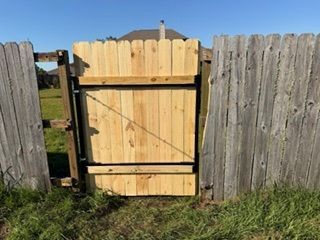 Wooden backyard gate between weathered fence panels, with grass and a house roof in the background