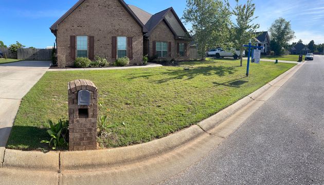 Brick house on a corner lot with a mailbox, driveway, and a road under a clear blue sky.