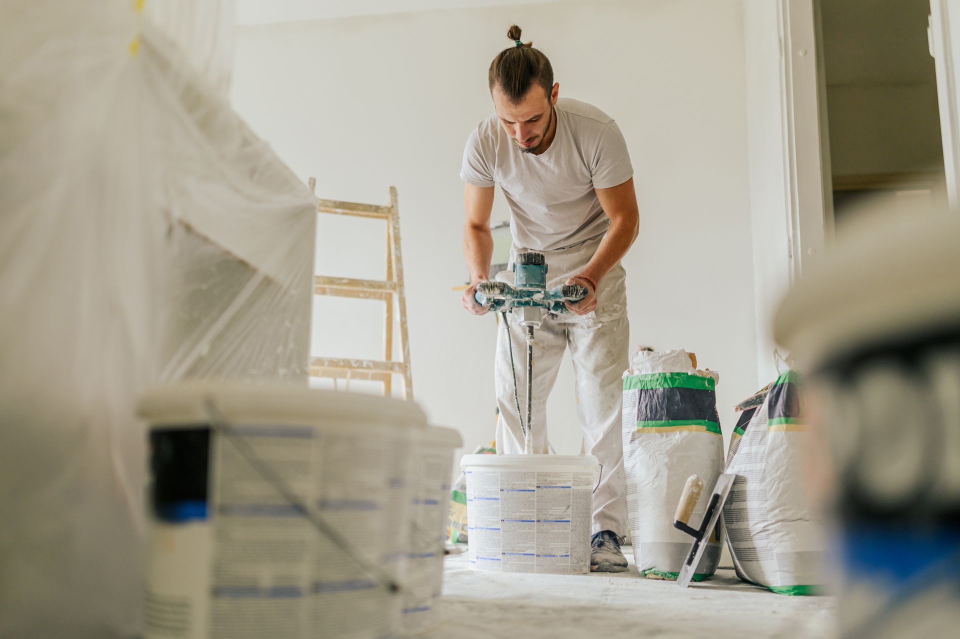 A man is mixing paint in a bucket in a room.