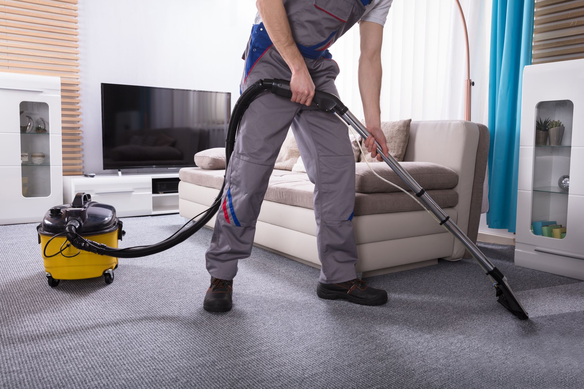 Person vacuuming a gray carpet in a living room, using a yellow vacuum cleaner.