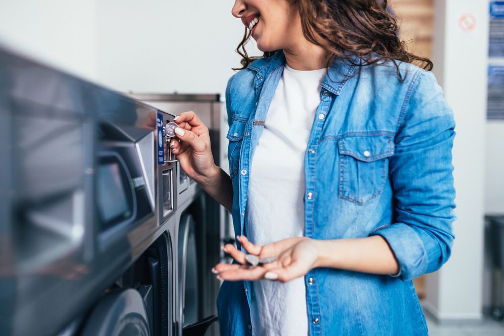 A Woman Is Putting Money Into A Washing Machine In A Laundromat — Buderim Laundrette In Buderim, QLD